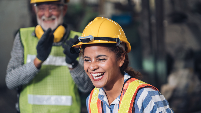DAVACO female employee wearing a yellow hard hat at a construction site, showing a bold company with diverse team members.