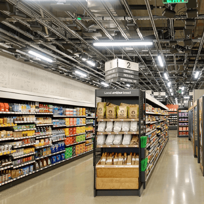 Bright grocery aisle inside Amazon Go, showing natural-colored food packaging for an eco-friendly feel, with bright beverages lining the side aisles.