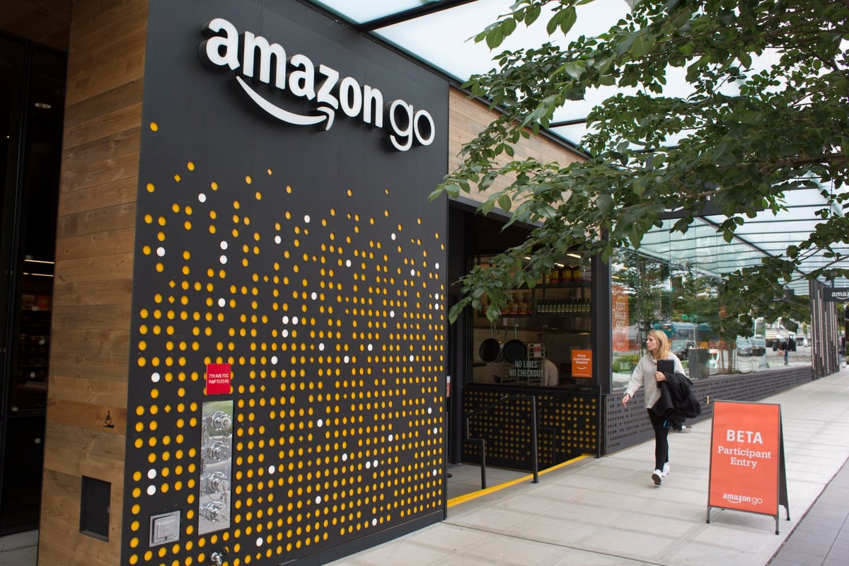 Amazon Go Storefront, showing a black entrance with bright orange dots, white logo and a female shopper.