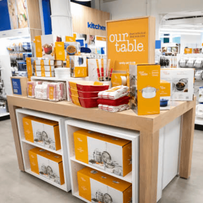 Kitchen section of a newly remodeled Bed Bath & Beyond store, with orange signage reading 'our table' featuring orange and red cookware.