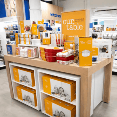 Kitchen section of a newly remodeled Bed Bath & Beyond store, with orange signage reading 'our table' featuring orange and red cookware.