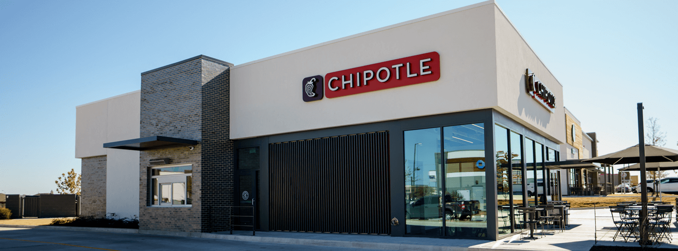 Exterior of a newly-remodeled Chipotle restaurant, showing brick and white exterior and floor to ceiling glass.