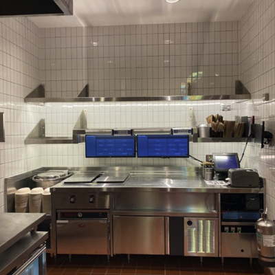 Bright white tile surrounding stainless steel kitchen equipment inside a Chipotle kitchen prep station.