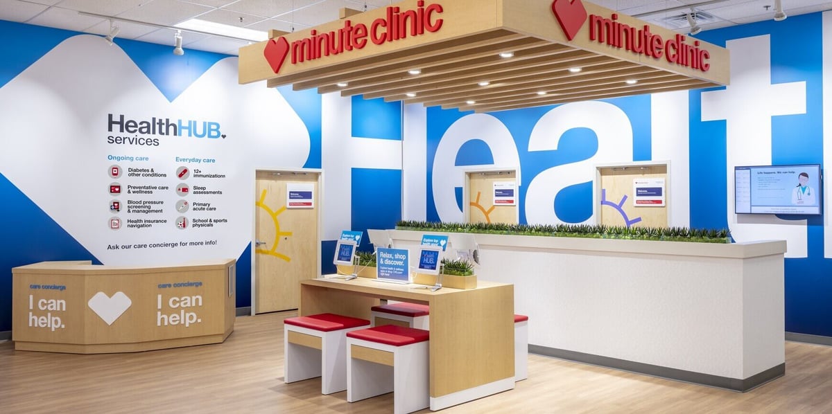 Entrance to a CVS HealthHUB, showing a wooden table with red and white stools in front of a blue wall painted with the word 'health'.
