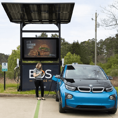 Woman standing with a blue, electric BMW car at an EOS charging station