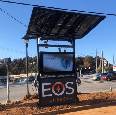 Black, solar-powered EOS charging station with large LCD screen for client entertainment at charging facility.
