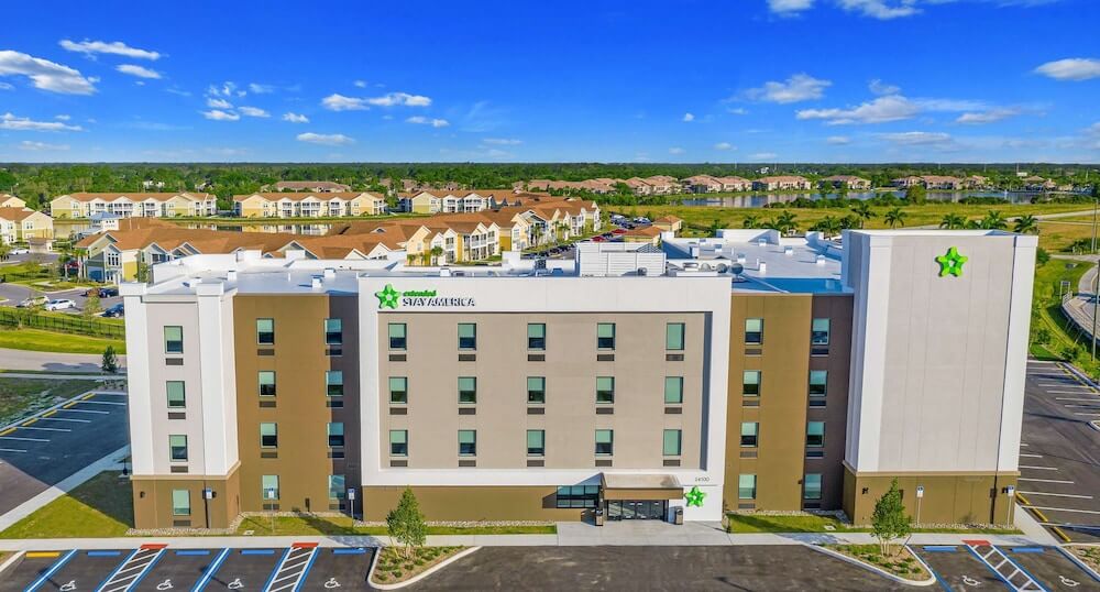 Aerial, exterior view of an Extended Stay America hotel, with a storefront in tan and brown with bright green logo.
