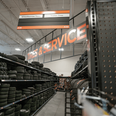 Aisle of tires on display with a bright orange sign reading 'tires & service' in a newly-remodeled Mills Fleet Farm store.