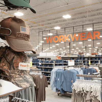 Brown and green baseball hats on display with men’s shirts featured on store racks in a Mills Fleet Farm store.