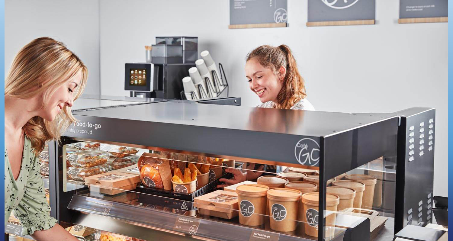 Two blonde females reaching into a Flexeserve food-to-go cooler, that is storing chilled food and beverages.