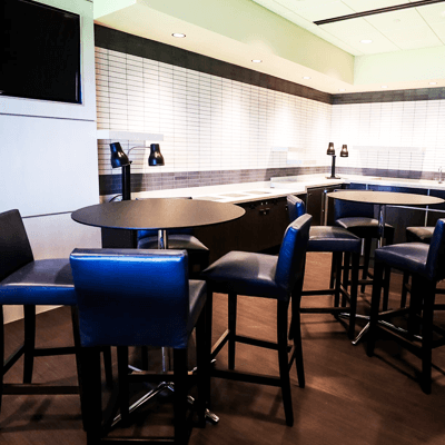 Wooden pub tables and chairs at the Bank of America Suite with a big screen tv and modern blue lights.