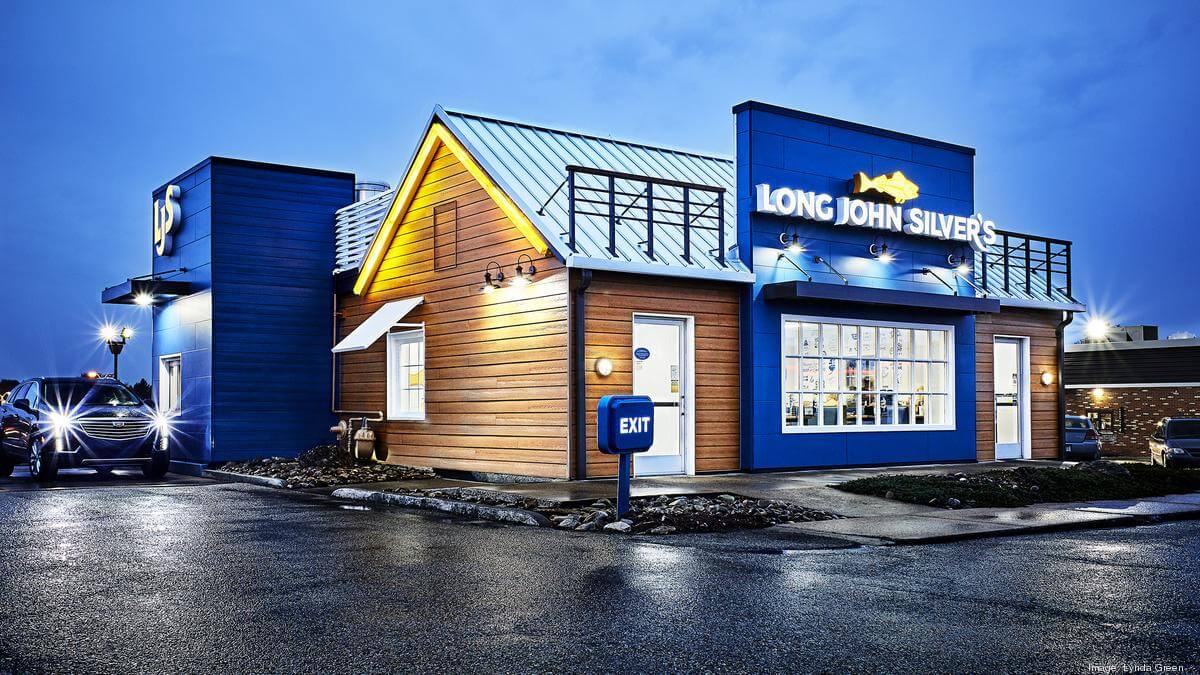 Night, front view of a newly remodeled Long John Silver's Restaurant, the entrance in bright blue and wood tones reminiscent of a pub by the harbor.
