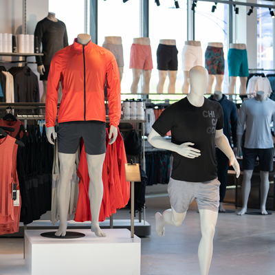 Running male mannequins posed with orange and black athletic clothing are featured inside a Lululemon store.