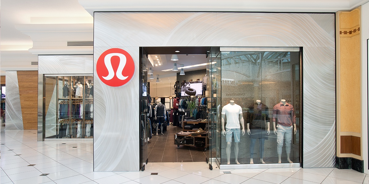 Storefront of a Lululemon store at a shopping mall, showing dark black borders of open glass doors into the modern athletic wear store.