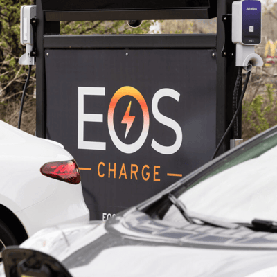 Cars lined up to charge at an EOS Charging station, shown by a black EOS charge sign.