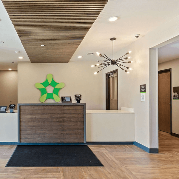 Front lobby of an Extended Stay America Hotel, showing white and oak fixtures and a bright green log, showcasing a project of 34 properties.