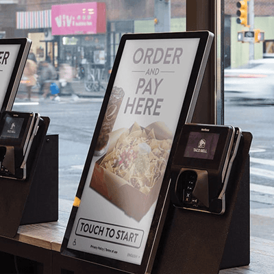 Closeup of a large LCD touchscreen reading 'Order and Pay Here' at a Taco Bell.
