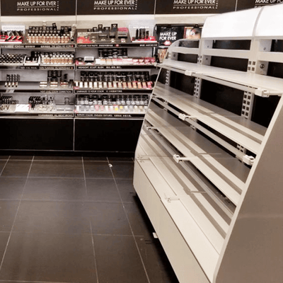 White metal cosmetics cabinet inside of a Sephora cosmetics store with colorful cosmetics on display in the background.