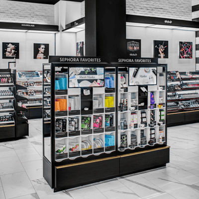 Black and white backlit cosmetics case inside a newly remodeled Sephora store, highlighting colorful cosmetics and fashion images on the walls.