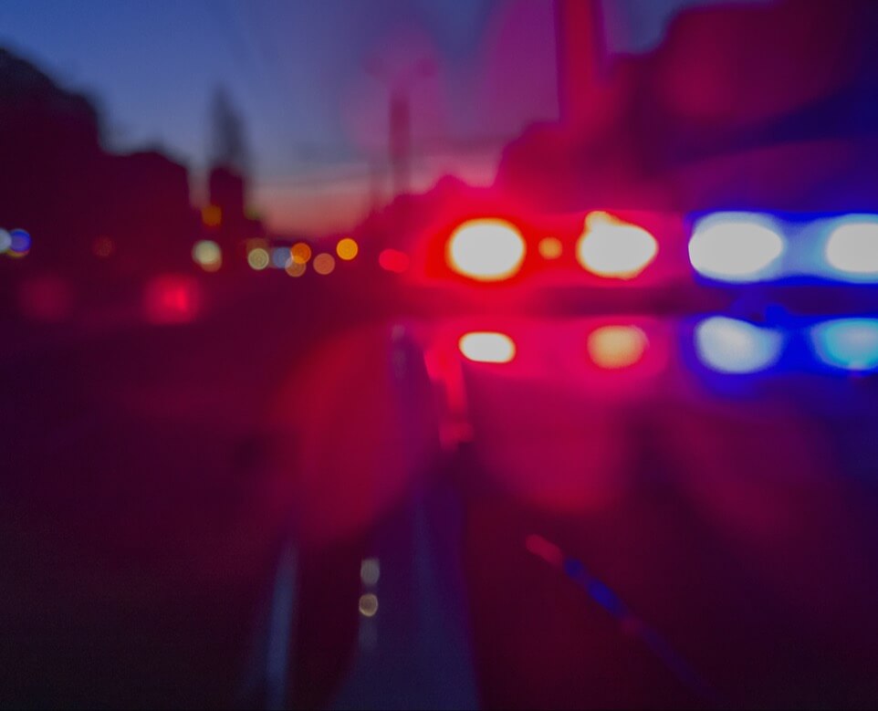 Blurred view of an emergency vehicle with red and blue lights, with a city in the background.