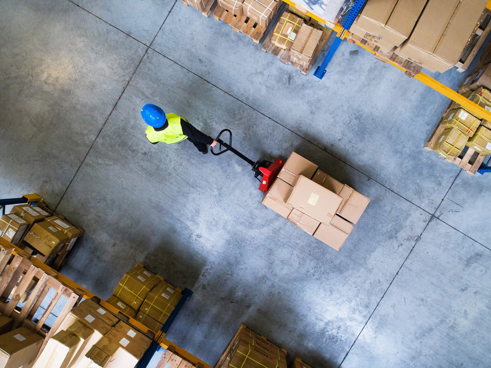 DAVACO logistics employee wearing yellow safety vest pulling a load of boxes in a warehouse.