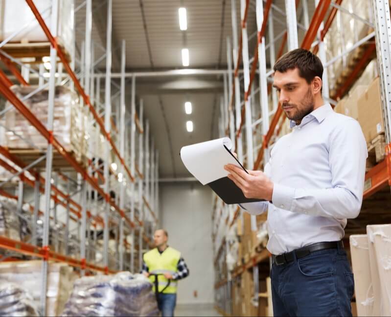Man in white business shirt checking a clipboard in a stocked warehouse. Showing DAVACO