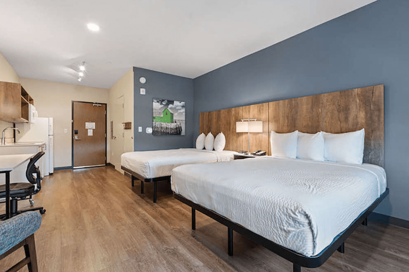 Interior of a modern, Extended Stay America hotel room with two queen beds, wooden floors and steel grey walls.