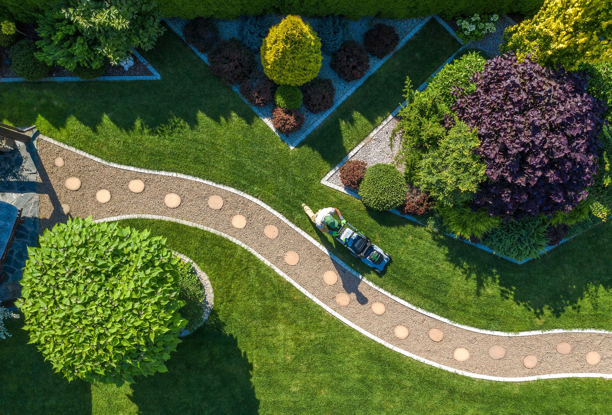 Aerial view of a DAVACO landscaping professional pushing a lawnmower through a perfectly groomed lawn surrounded by lush greenery and foliage.
