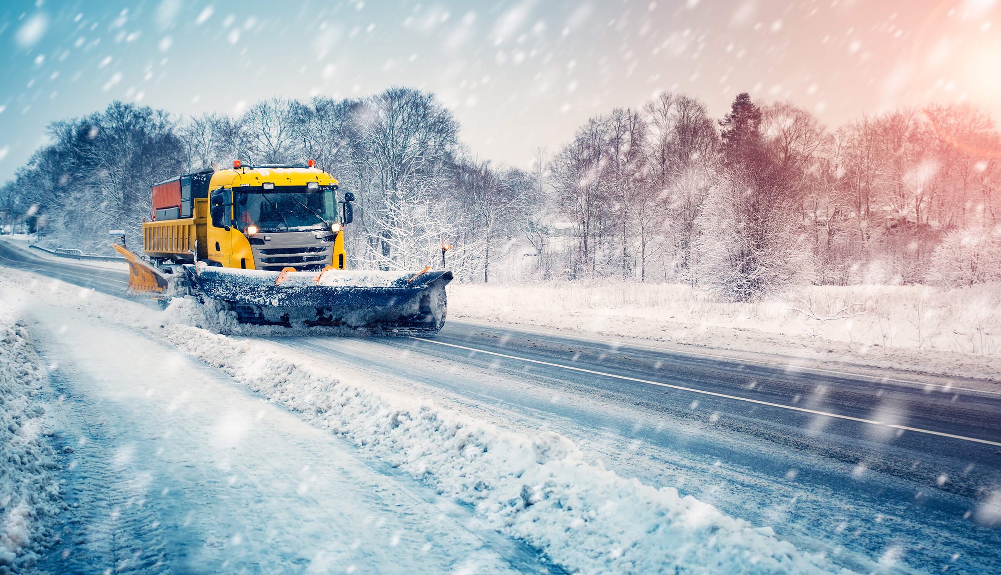 Bright yellow snowplow in a thick snowstorm plowing a highway.