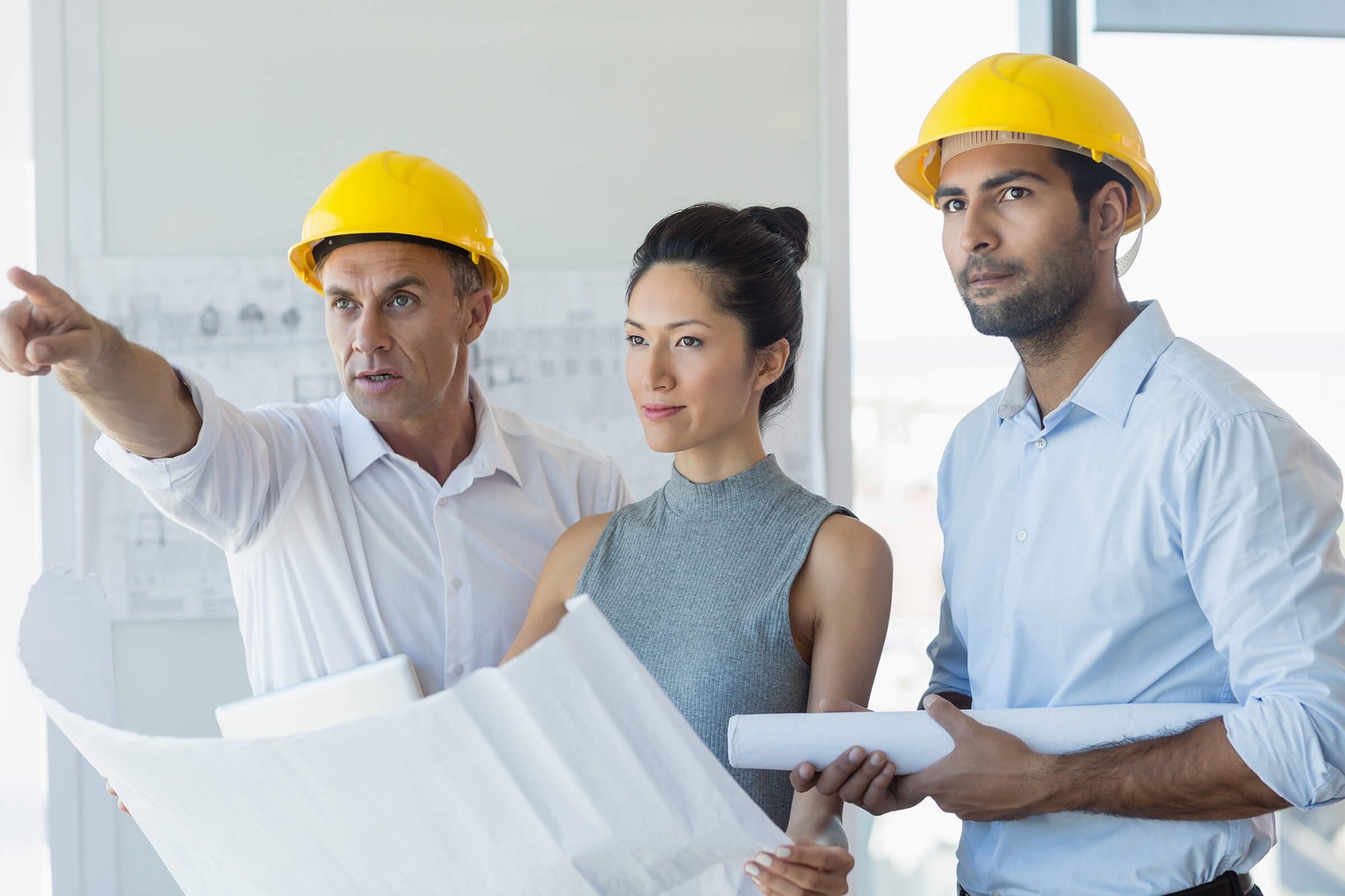 Three DAVACO employees discussing architecture plans, one pointing, all wearing hard hats.