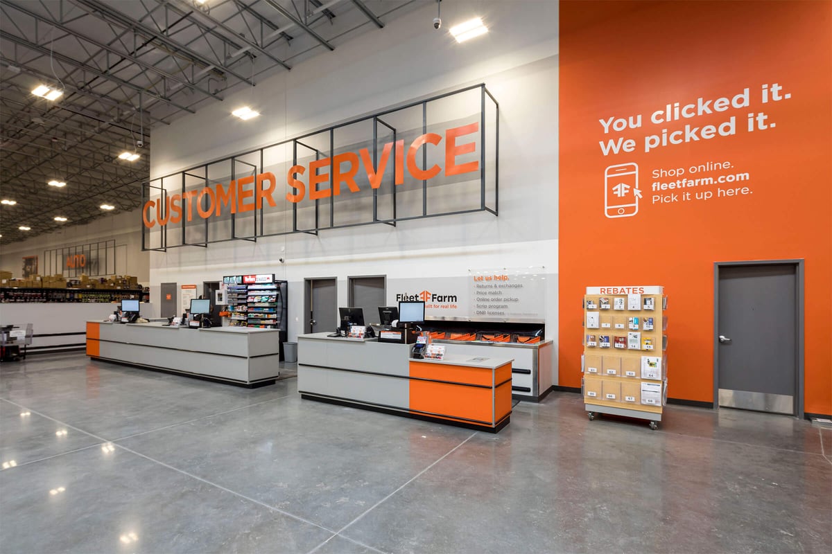 Customer service counter at a Mills Fleet Farm store, with bright orange walls and signage and steel backdrops.