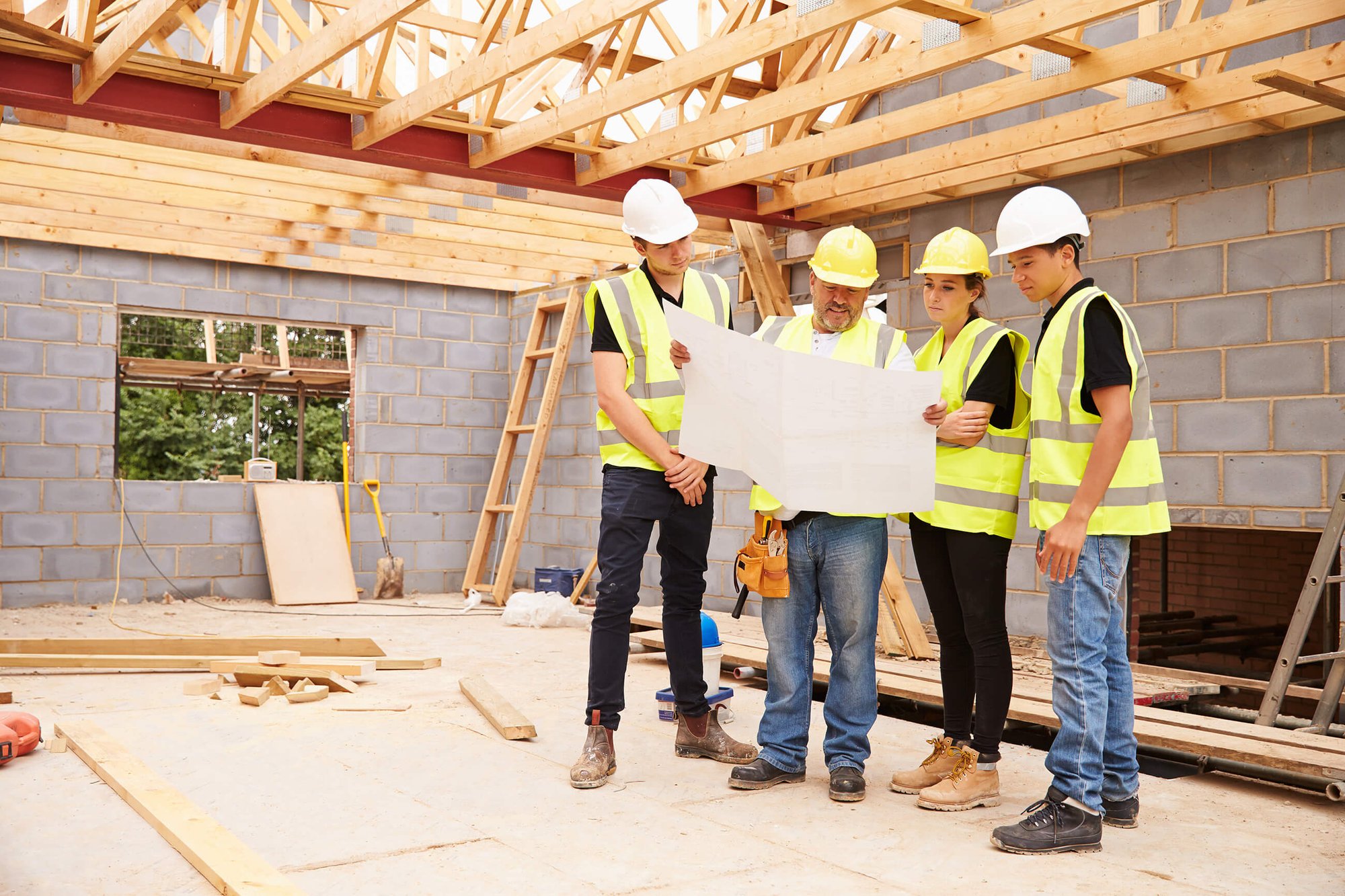 Four DAVACO construction team members wearing hard hats and reflective vests viewing architectural drawings inside of a construction site.