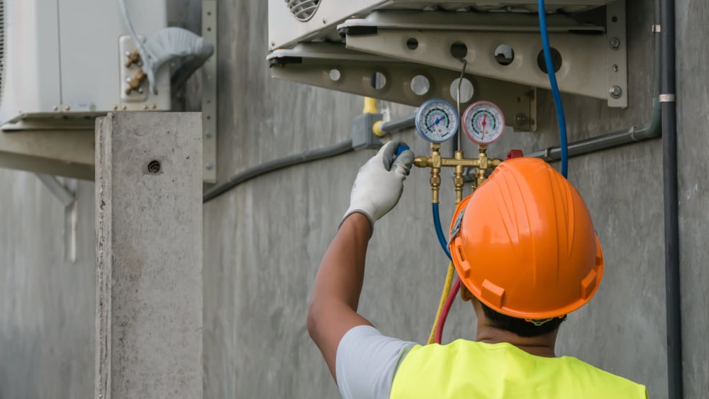 Vendor Button: Man wearing a hard hat, working on an HVAC unit outside