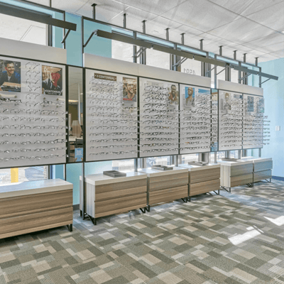 Wall of new eyewear displayed at a Stanton Optical My Eye Lab store, with earth-tone carpet, wooden seating and bright blue walls.