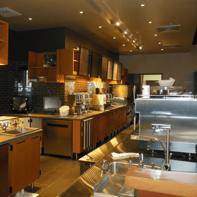 Newly remodeled prep area of a Starbucks coffee shop, with steel and wooden accents, warm lighting and earth-toned walls and flooring.