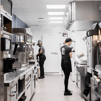 Kitchen of a Taco Bell Restaurant, with two employees at work at the stainless steel appliances that line the prep area.