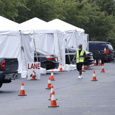 Row of white tents filled with vehicles, and an employee wearing a yellow safety vest walking the grounds of the TDEM Covid-19 testing site.