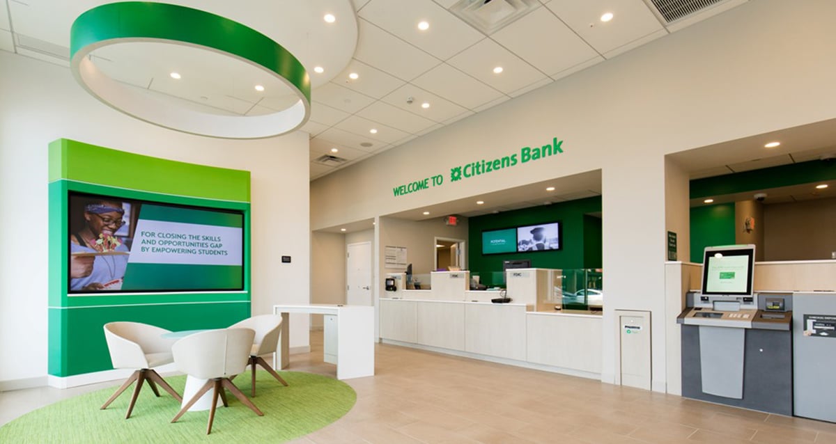 Interior lobby of Citizen's Bank Charlestown, showing bright white interiors with green accents. A large sign reads 'Welcome to Citizens Bank'.